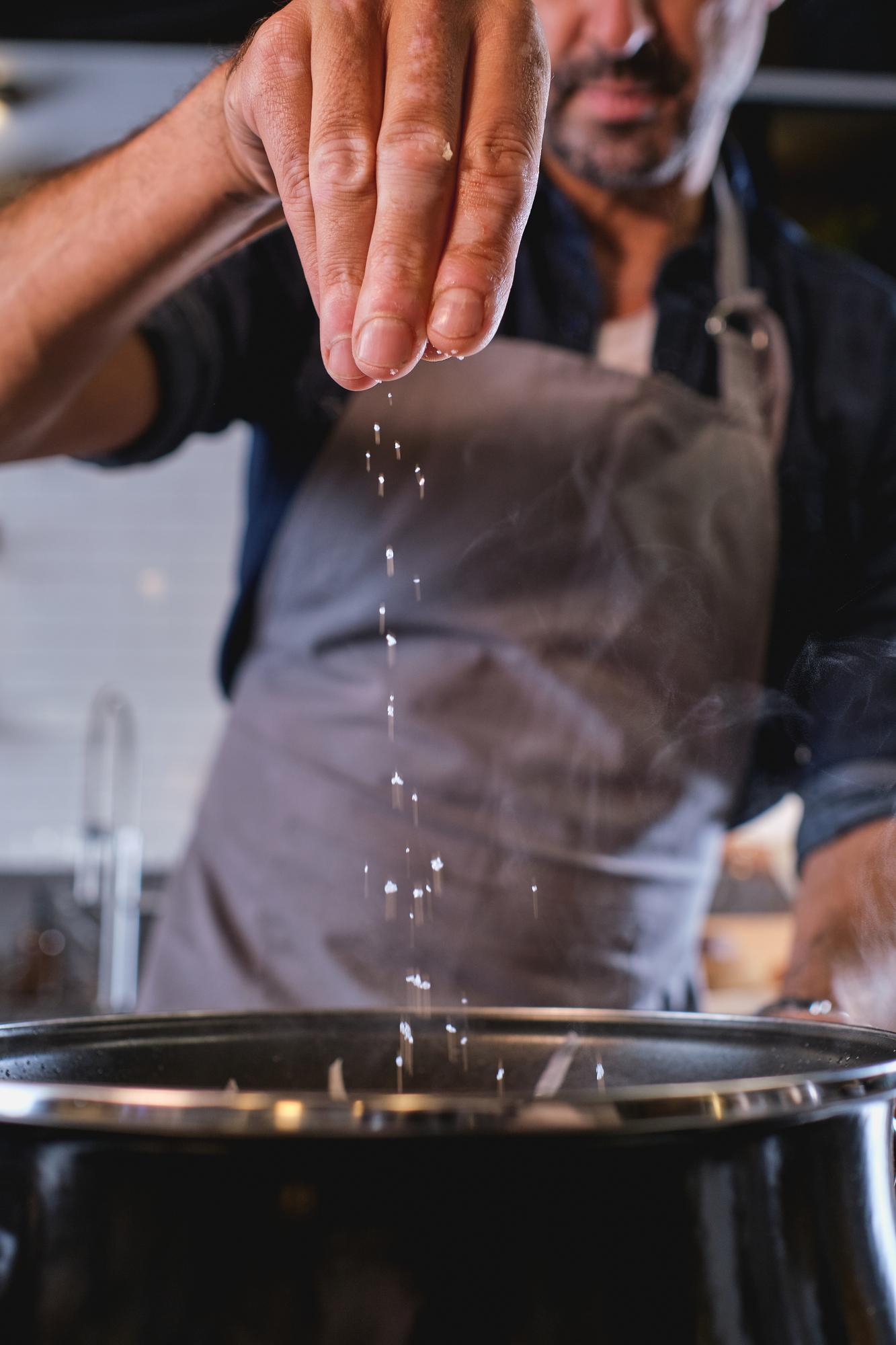 Chef adjusting seasoning over a pan